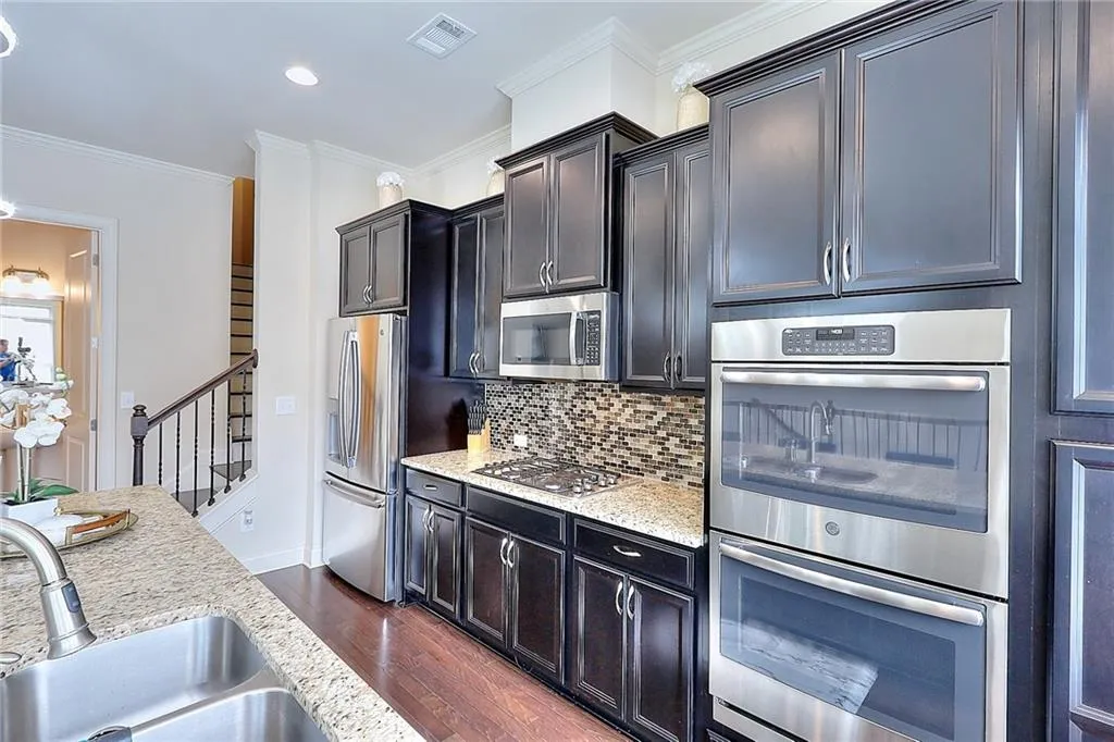 Kitchen with stainless steel appliances, dark wood-style flooring, tasteful backsplash, light stone countertops, and crown molding