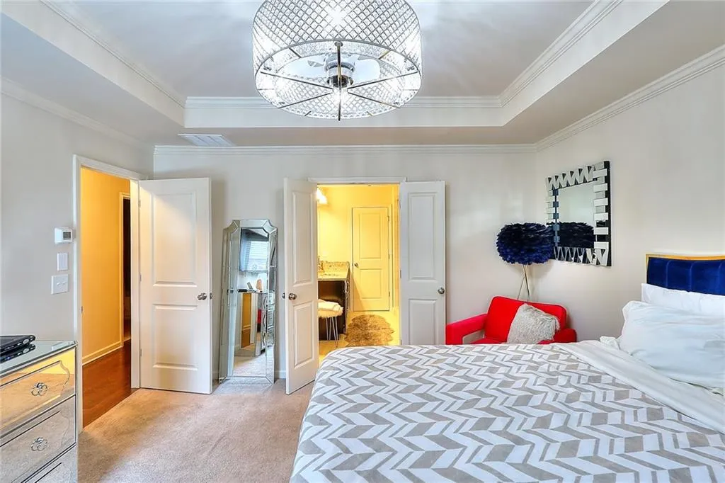 Bedroom featuring light colored carpet, a raised ceiling, a chandelier, and ornamental molding