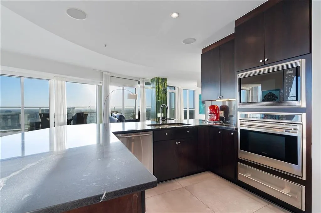 Kitchen with dark brown cabinetry, stainless steel appliances, a warming drawer, light tile patterned flooring, and dark stone countertops Kitchen with dark brown cabinetry, stainless steel appliances, a warming drawer, light tile patterned flooring, and dark stone countertops