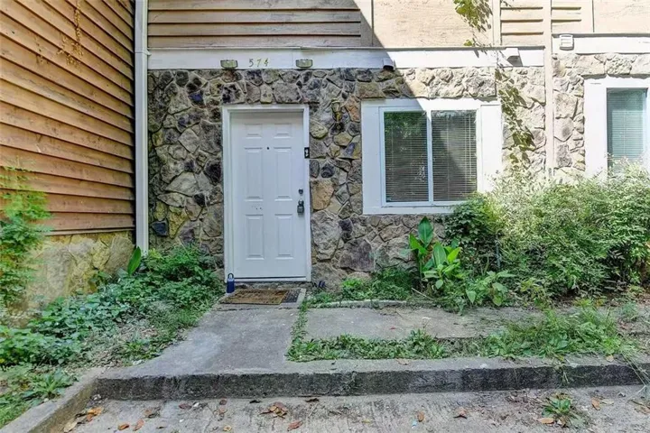 Exterior featuring stone cladding, horizontal wood siding, a white entry door, and white-framed windows