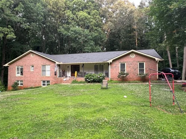 Brick exterior featuring a covered front porch and mature trees