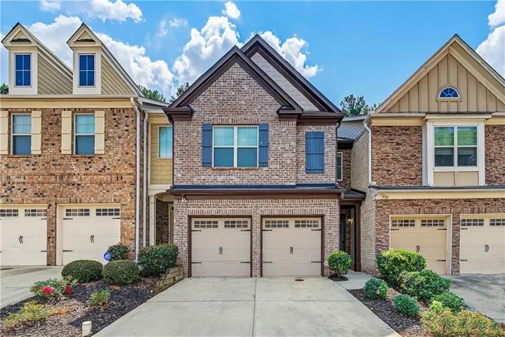 Brick exterior with a dark-pitched roof, dual garage doors, decorative window shutters, and a concrete driveway