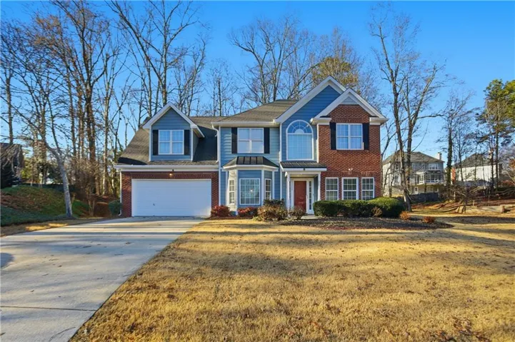 View of front facade with driveway, brick siding, roof with shingles, and a front yard