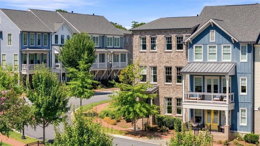 Beautiful END UNIT Townhome exterior featuring board and batten siding, brick facade, covered balcony, and mature landscaping with a side yard area