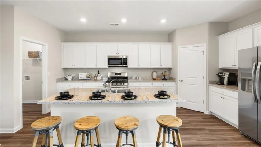 Kitchen featuring white cabinetry, stainless steel appliances, a center island with countertop seating, wood-finish flooring, and recessed lighting