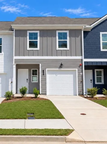 Two-story exterior with board and batten siding, attached garage, concrete driveway, and manicured landscaping