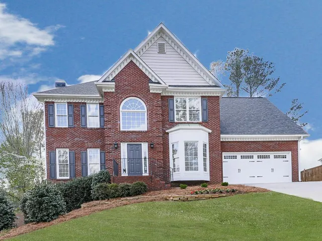 View of front facade featuring brick siding, a front yard, an attached garage, and driveway