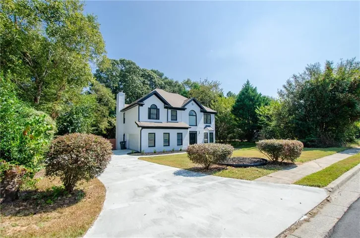 Traditional-style home with a chimney, driveway, a front lawn, a garage, and view of wooded area