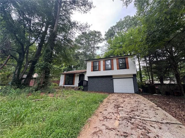 Split-level exterior with white siding and dark lower-level facade, featuring a white garage door, black front door, and natural wood-look shutters