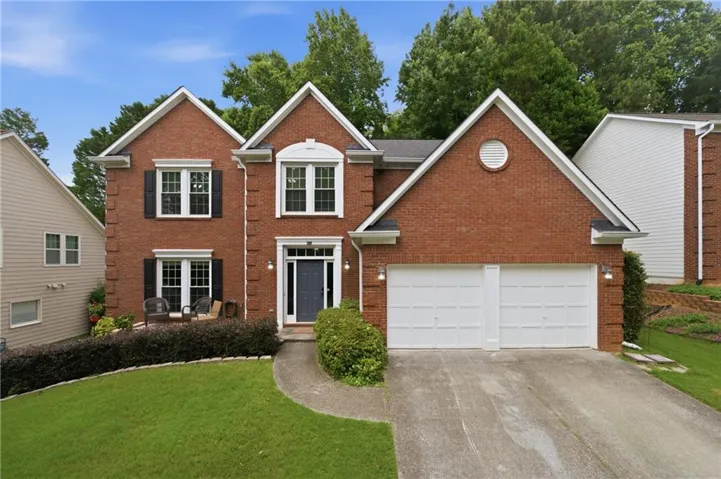 Brick exterior featuring a two-car garage, manicured lawn, and a concrete driveway