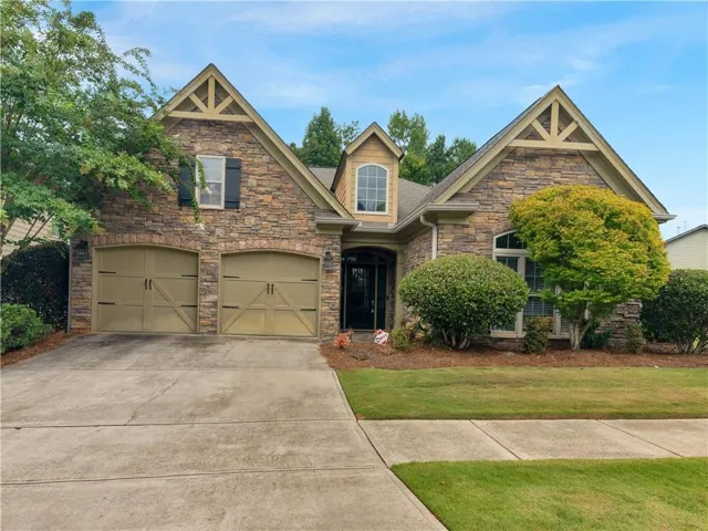 Stone facade with wood-look gable accents, featuring a two-car garage with arched doors, a covered entry, and established perimeter landscaping