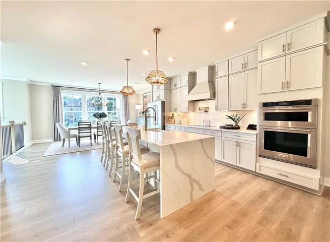 Gourmet kitchen with light-toned cabinetry, stainless steel appliances, a large center island with a waterfall edge, and wood-finish flooring
