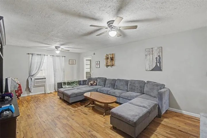 Spacious living area featuring wood-finish flooring, two ceiling fans with integrated lighting, and light-toned wall paint