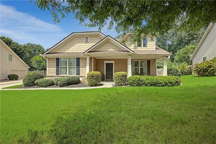 Two-story residence featuring a covered front porch, dormer window, and mature front landscaping