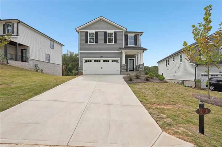 Craftsman-style house featuring an attached garage, a front lawn, driveway, and stone siding