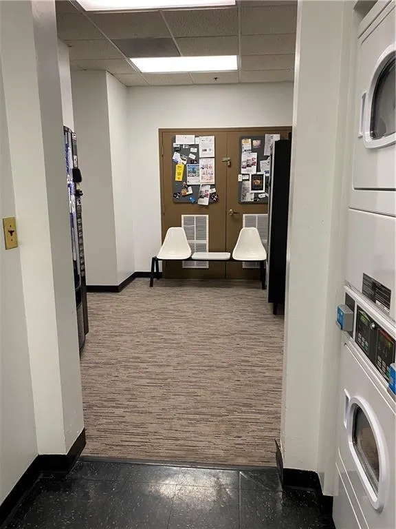 Hallway featuring stacked washer and dryer, a paneled ceiling, visible vents, and baseboards