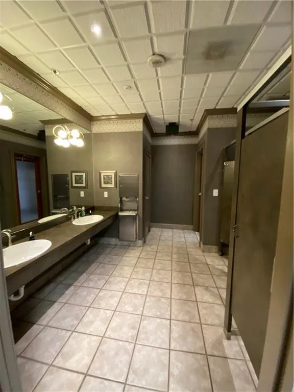 Bathroom featuring double sink, baseboards, crown molding, and tile patterned floors