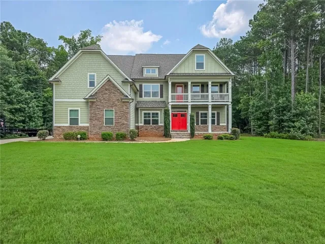 Striking Colonial-style residence featuring a brick and siding exterior with a prominent red entry door, multiple gabled rooflines, and a covered front porch with columns