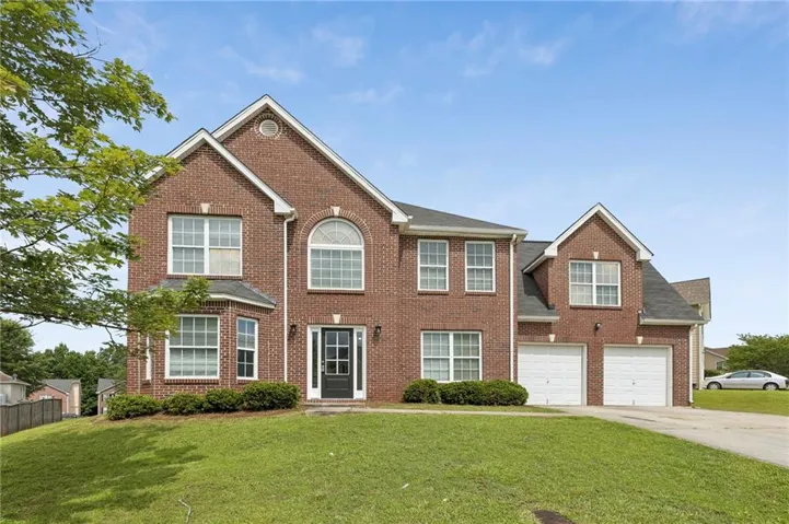 Two-story brick exterior with a prominent arched window, bay window feature, dual white garage doors, and a dark front entry door
