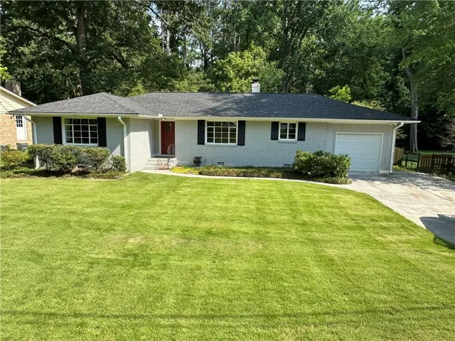 Ranch-style residence featuring light gray brick exterior, dark gray shingle roof, black window shutters, red entry door, and an attached single-car garage