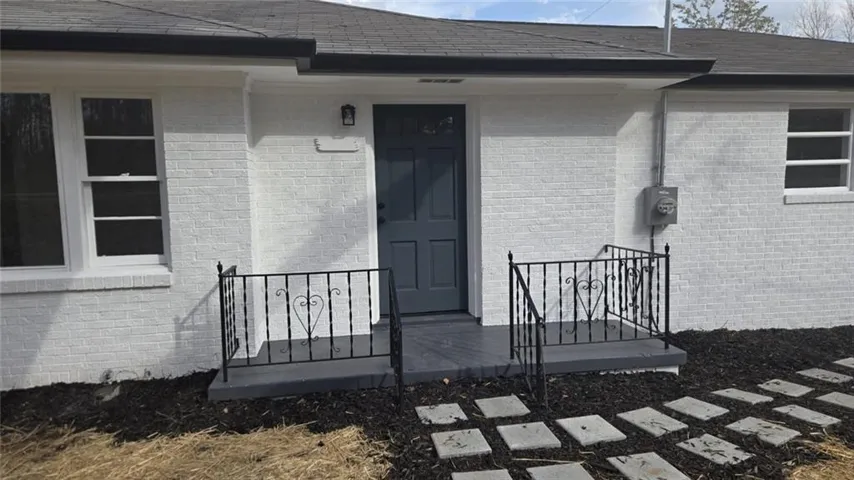 White brick exterior with a dark gray entry door, black wrought iron railings, dark gray porch, and a stepping stone path