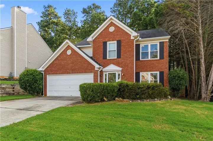 Brick exterior with a peaked roofline, an attached two car garage, a bay window, and a manicured lawn