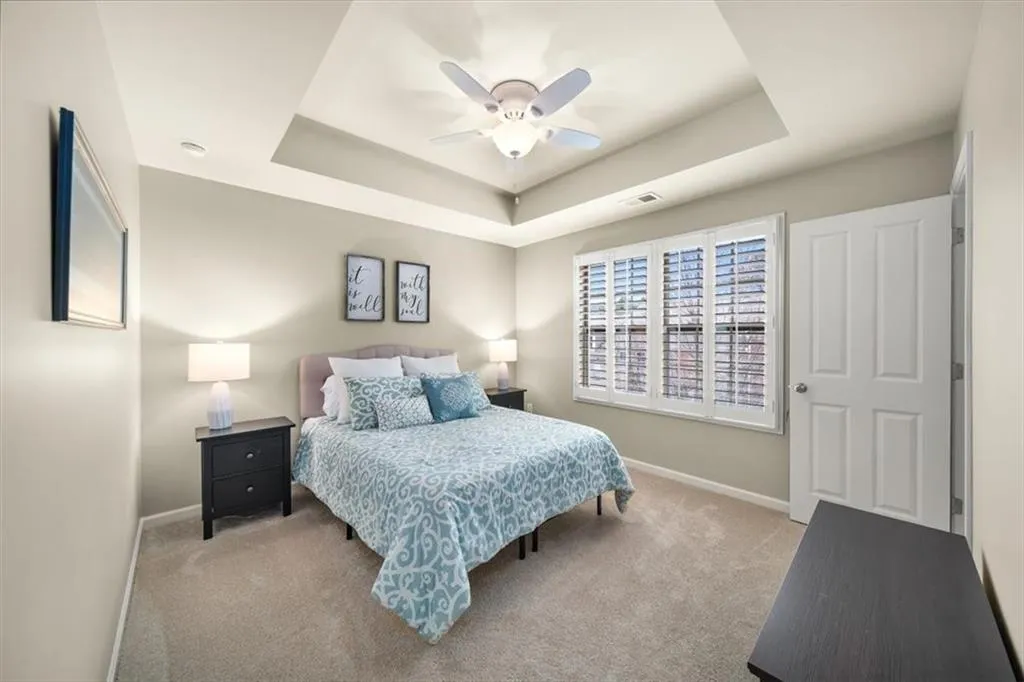 Bedroom with light carpet, a tray ceiling, and ceiling fan