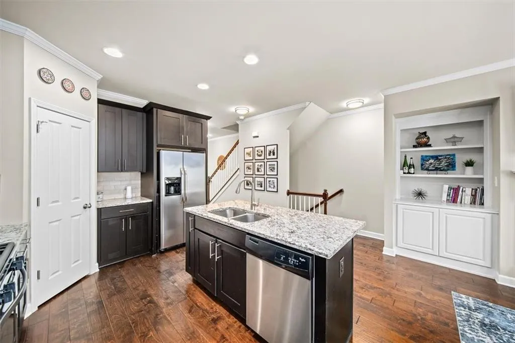 Kitchen featuring appliances with stainless steel finishes, dark hardwood / wood-style floors, sink, light stone counters, and a center island with sink