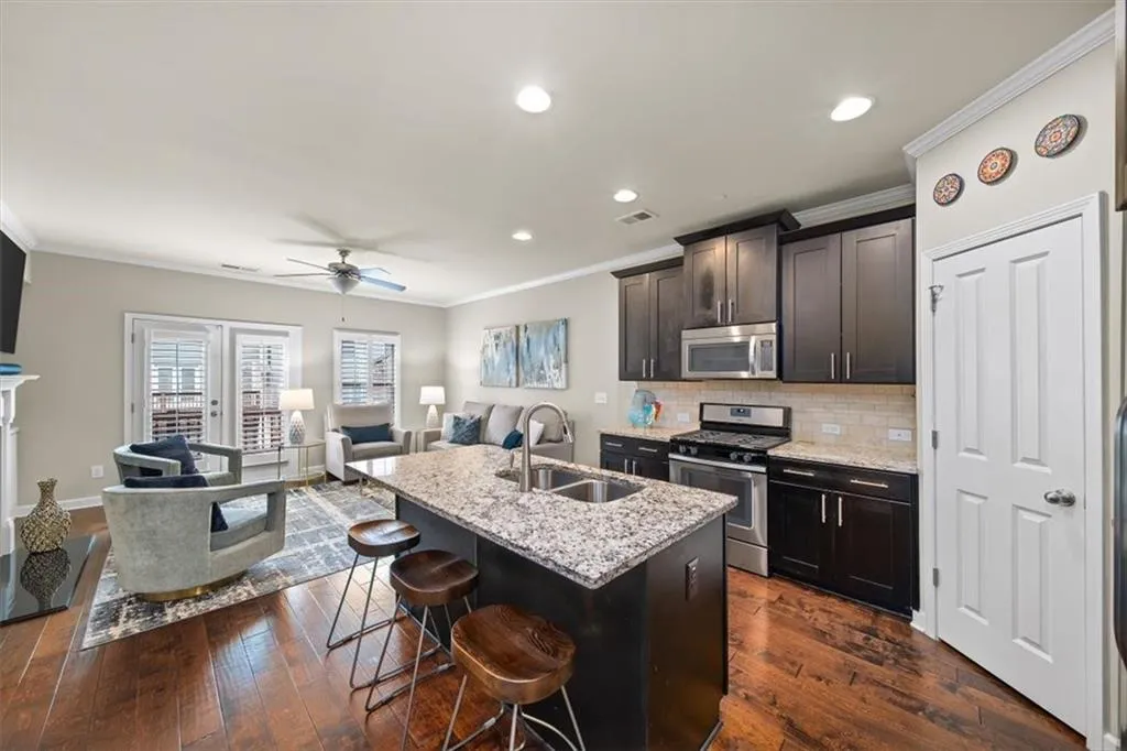 Kitchen with sink, a center island with sink, appliances with stainless steel finishes, a kitchen breakfast bar, and light stone countertops