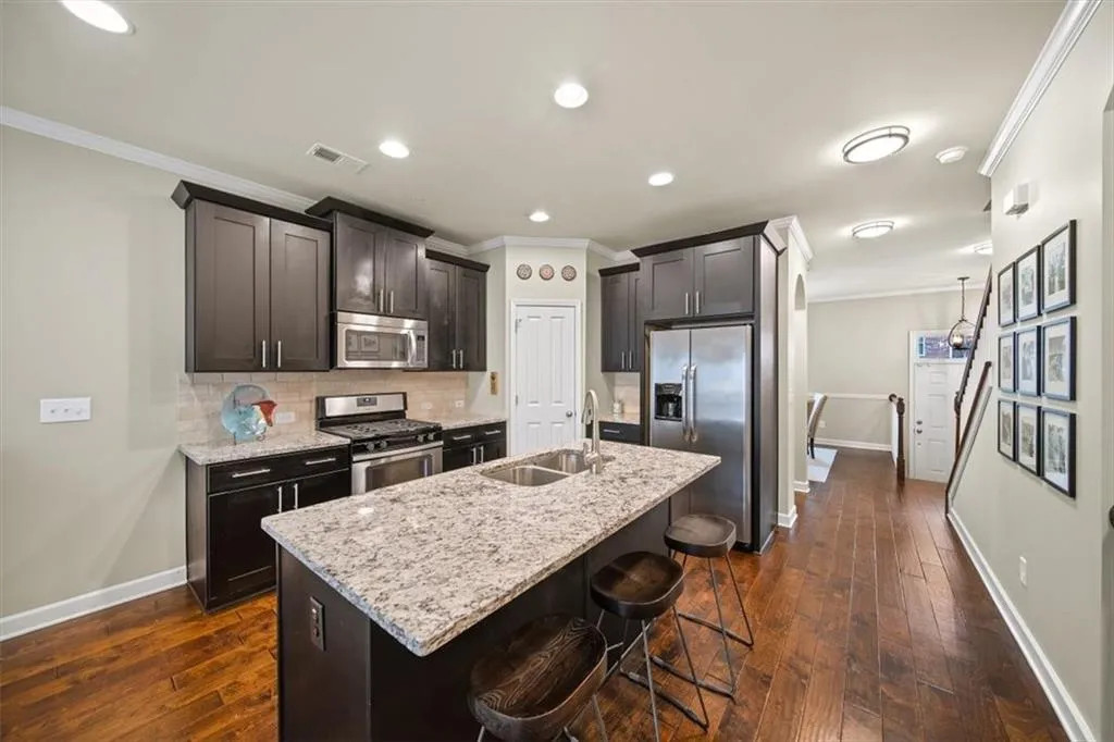 Kitchen featuring a breakfast bar, sink, light stone counters, appliances with stainless steel finishes, and an island with sink