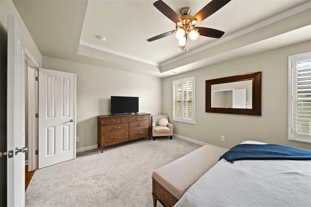 Carpeted bedroom featuring ceiling fan, ornamental molding, and a tray ceiling