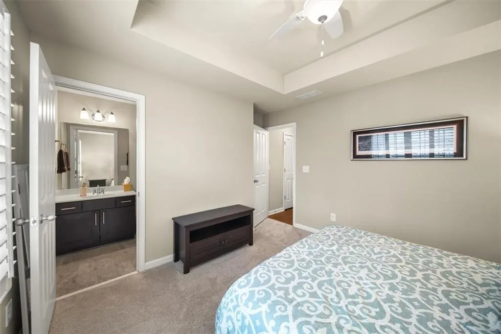 Bedroom with connected bathroom, sink, light colored carpet, a raised ceiling, and ceiling fan