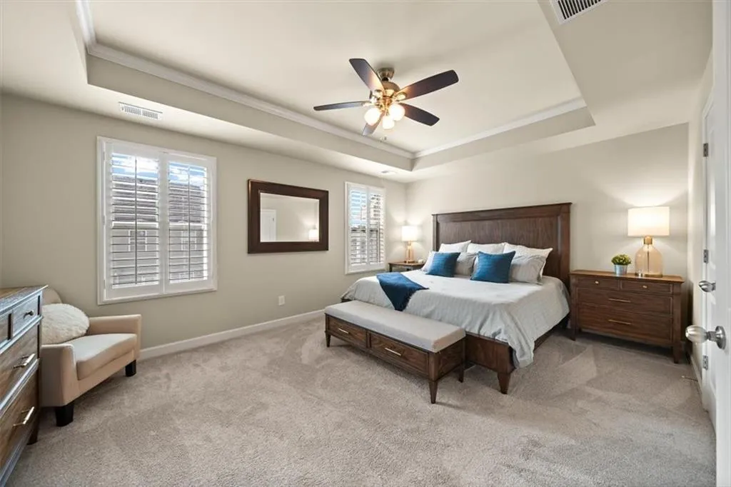 Bedroom with light carpet, crown molding, multiple windows, and a raised ceiling