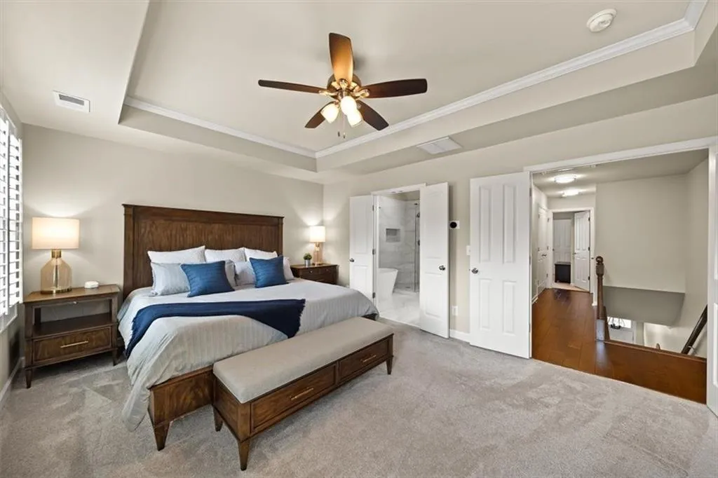 Carpeted bedroom with a raised ceiling, ornamental molding, ceiling fan, and ensuite bath
