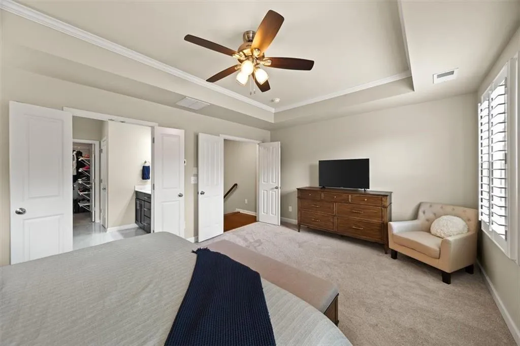 Bedroom featuring ornamental molding, a walk in closet, light colored carpet, ceiling fan, and a tray ceiling
