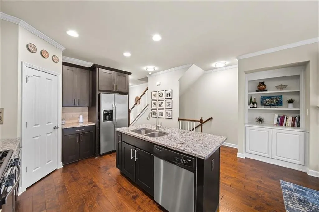 Kitchen featuring sink, dark wood-type flooring, appliances with stainless steel finishes, a kitchen island with sink, and light stone counters