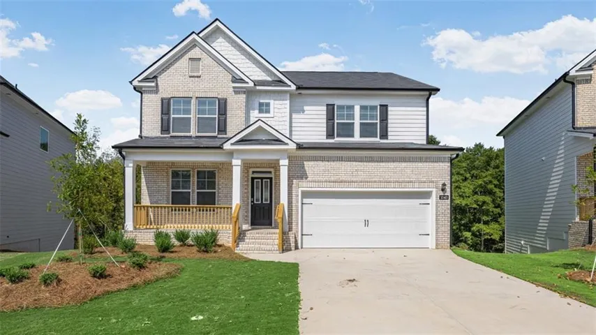 Two-story residence featuring light-colored brick and white siding, an attached two-car garage, a covered front porch with wood railings, and a concrete driveway