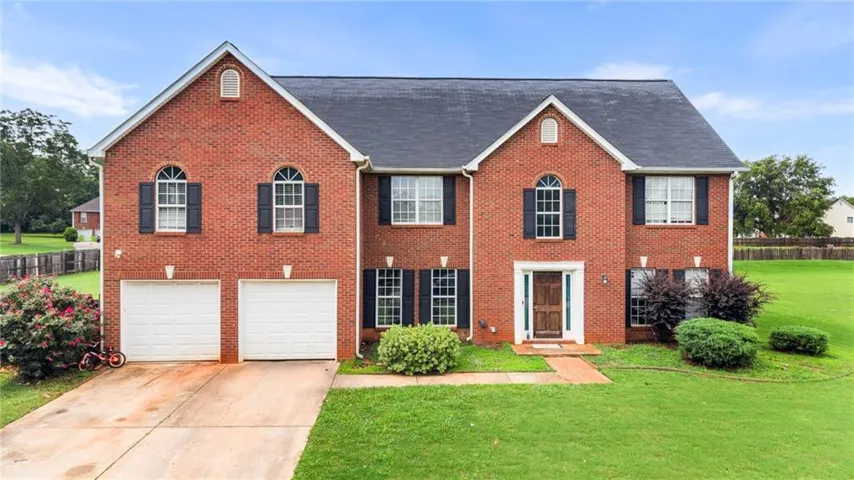 Brick exterior featuring a dark roofing system, two-car garage, and a central entry with a dark wood-finish door
