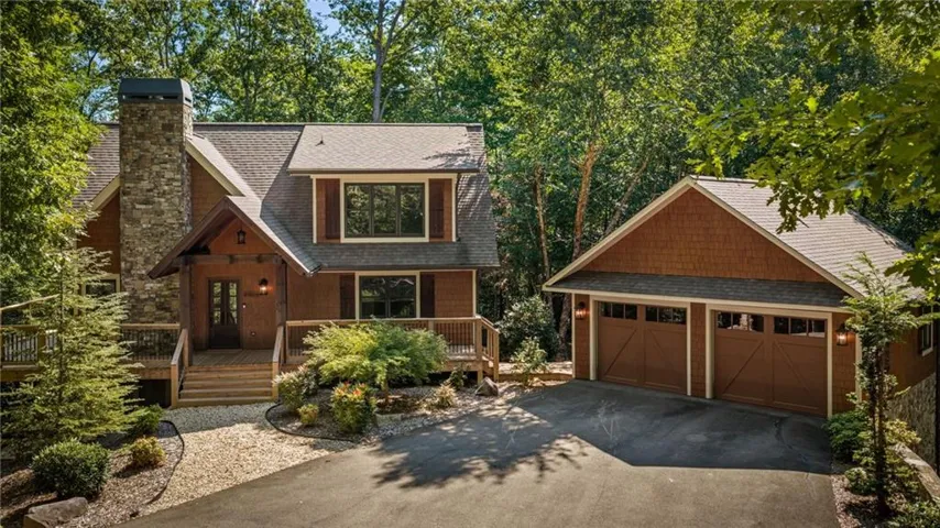 Stone chimney with natural wood siding, multi-level decking, gabled roofline, and a detached two-car garage with carriage-style doors