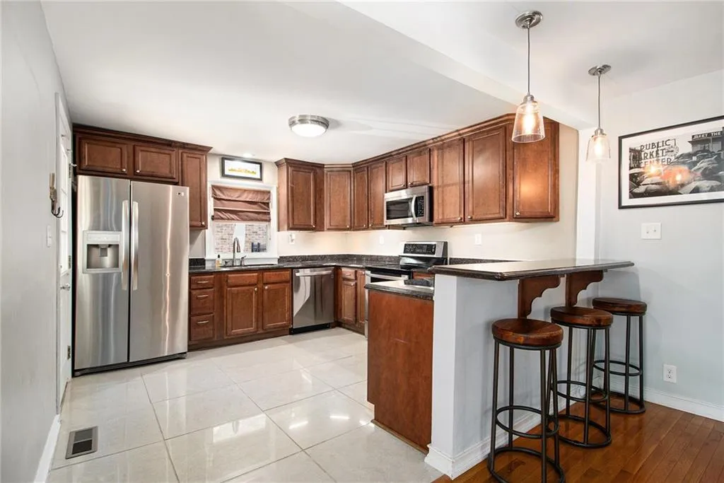 Kitchen with appliances with stainless steel finishes, a breakfast bar, a peninsula, pendant lighting, and brown cabinetry