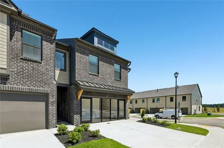 Brick and siding exterior with dark-framed windows, metal roof accents, and a ground-level garage