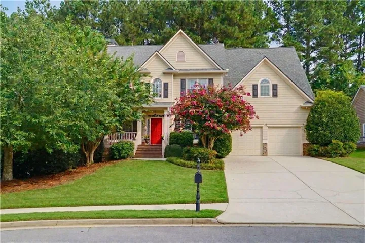 Traditional-style residence with a red entry door, symmetrical gabled rooflines, two-car garage, and mature landscaping