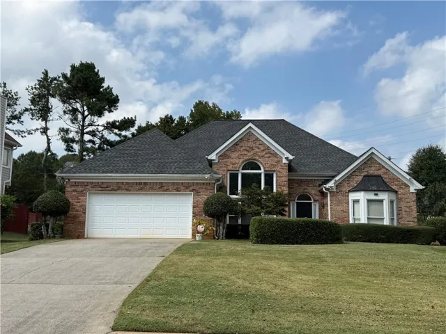 Brick exterior with a dark shingle roof, arched windows, a white garage door, and a bay window