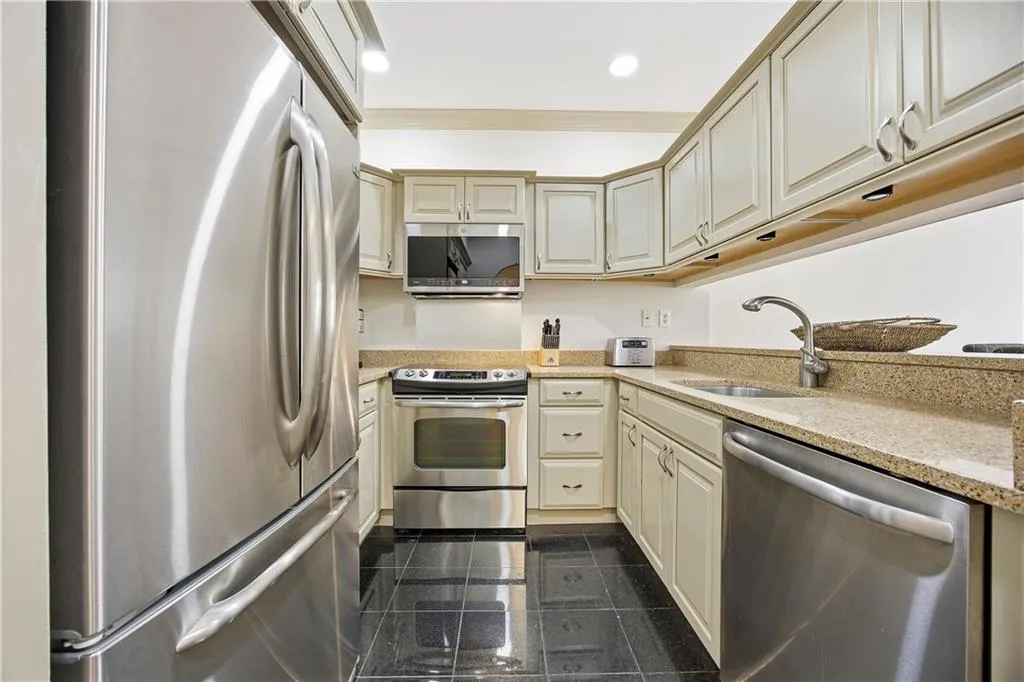 Kitchen with appliances with stainless steel finishes, light stone countertops, granite tiled floors, recessed lighting, and ornamental molding