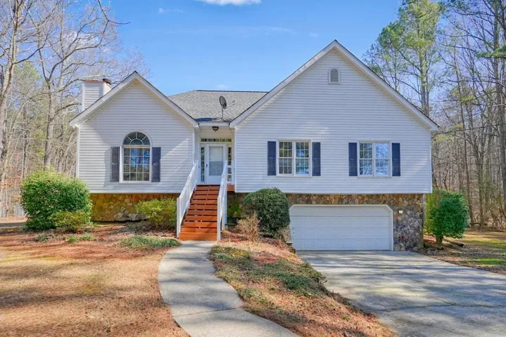 Ranch-style house with stone siding, a garage, a chimney, driveway, and a shingled roof