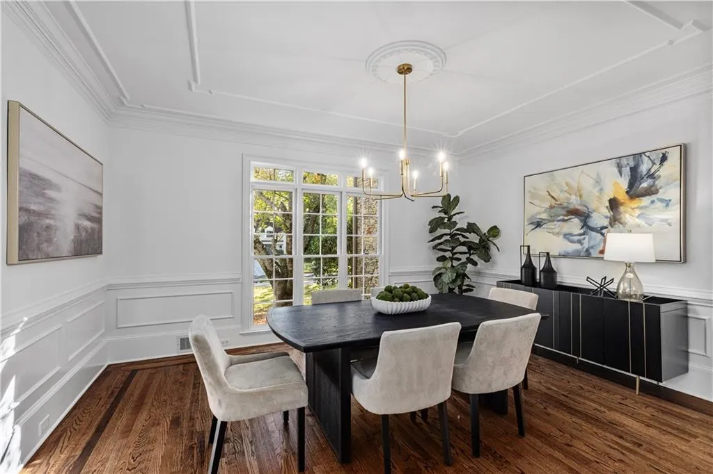 Dining room with a decorative wall, a wainscoted wall, dark wood-style flooring, a chandelier, and ornamental molding