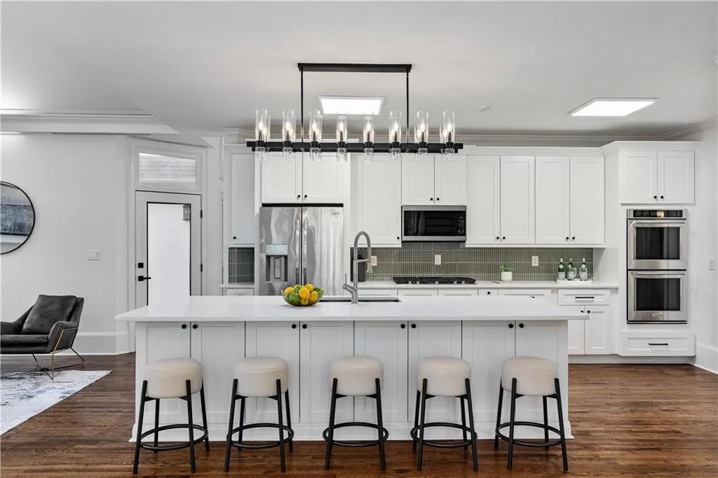 Kitchen with white cabinetry, a kitchen bar, decorative backsplash, appliances with stainless steel finishes, and a large island with sink