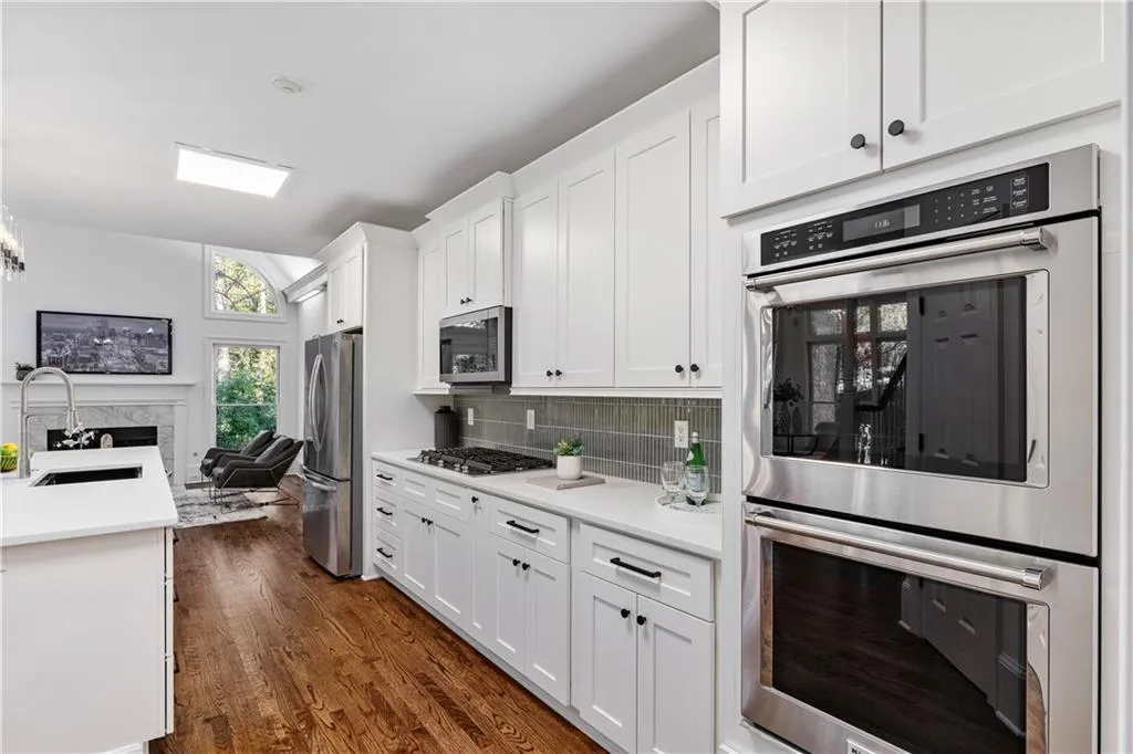 Kitchen featuring appliances with stainless steel finishes, white cabinetry, tasteful backsplash, light stone countertops, and dark wood finished floors