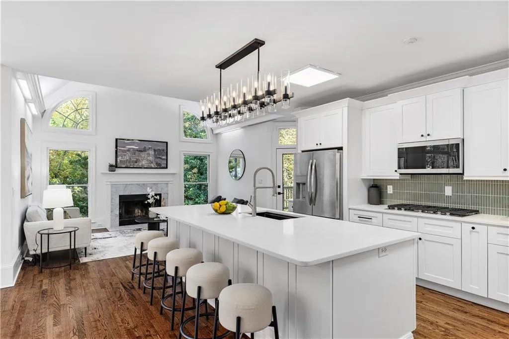 Kitchen with white cabinets, decorative backsplash, an island with sink, stainless steel appliances, and dark wood finished floors