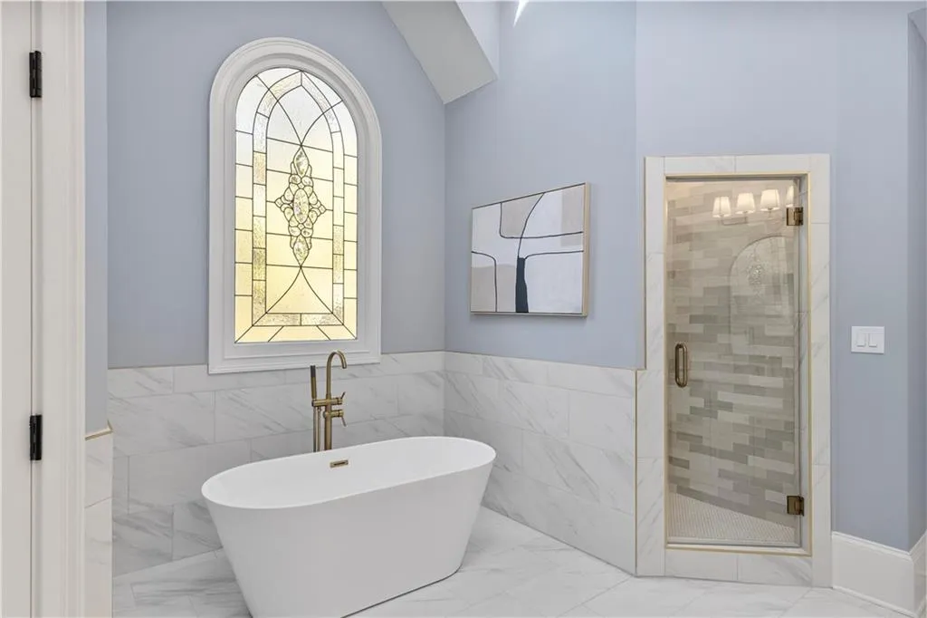 Full bathroom featuring a freestanding bath, a stall shower, marble look tiles, tile walls, and a wainscoted wall